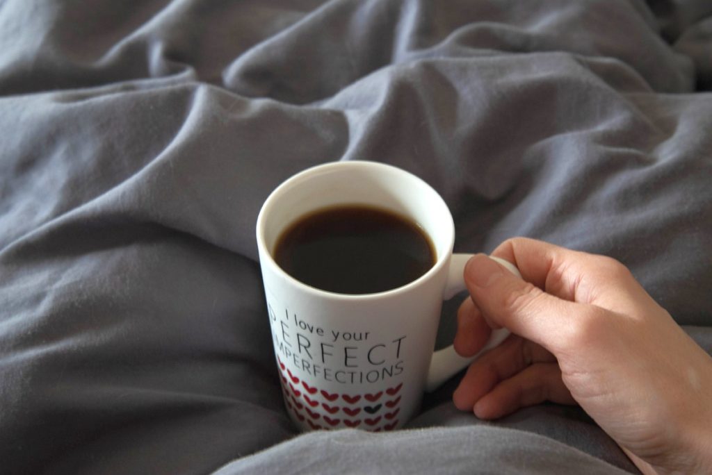 Hand holding a white cup iwth black coffee.