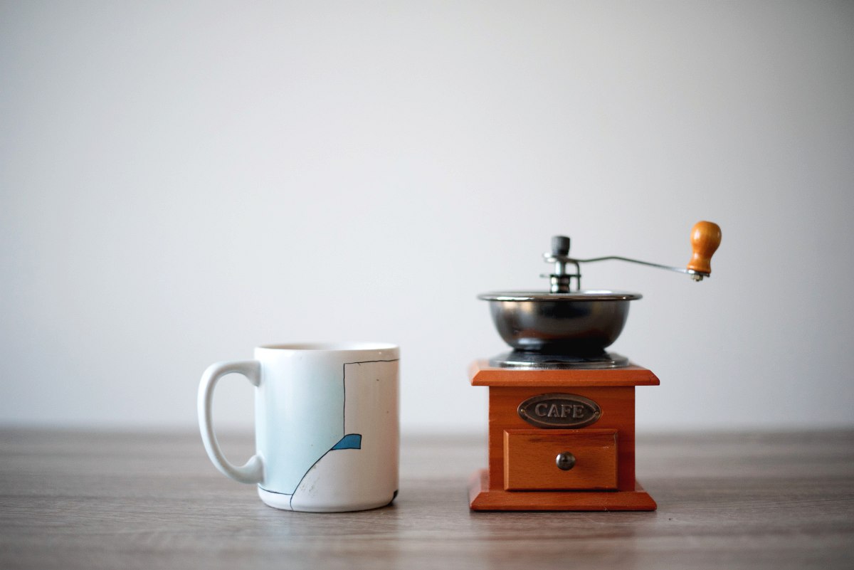 Photo of a coffee cup and an old school coffee grinder next to it.